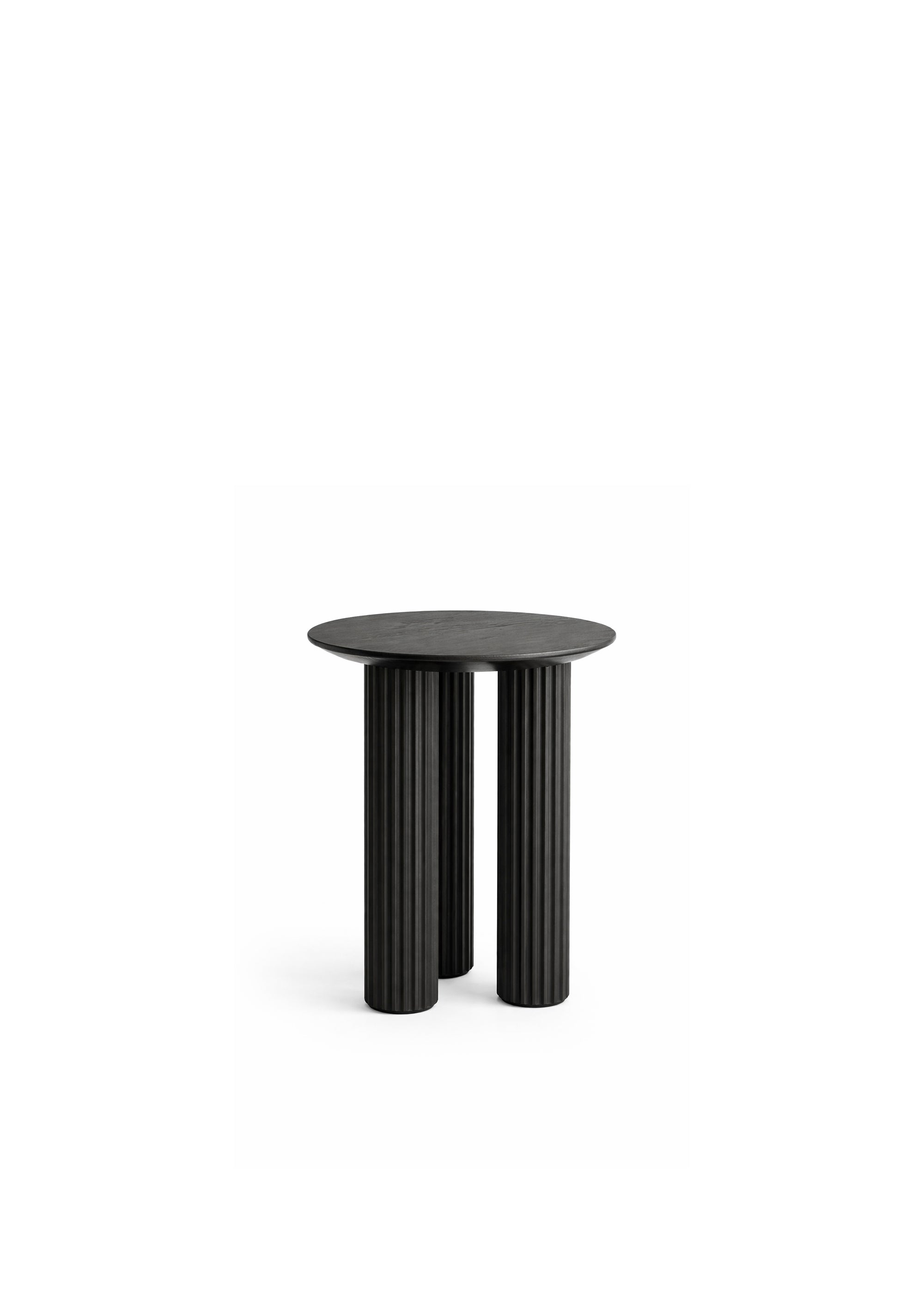 A round wooden side table with three grooved cylindrical legs placed beside a sofa in a bright living room