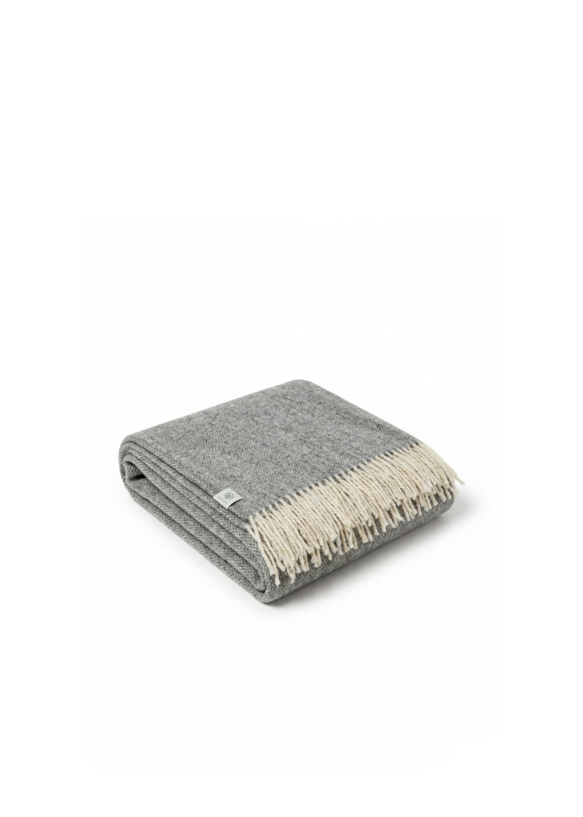 Couverture roulée en laine grise et crème avec des franges reposant sur un canapé beige texturé.