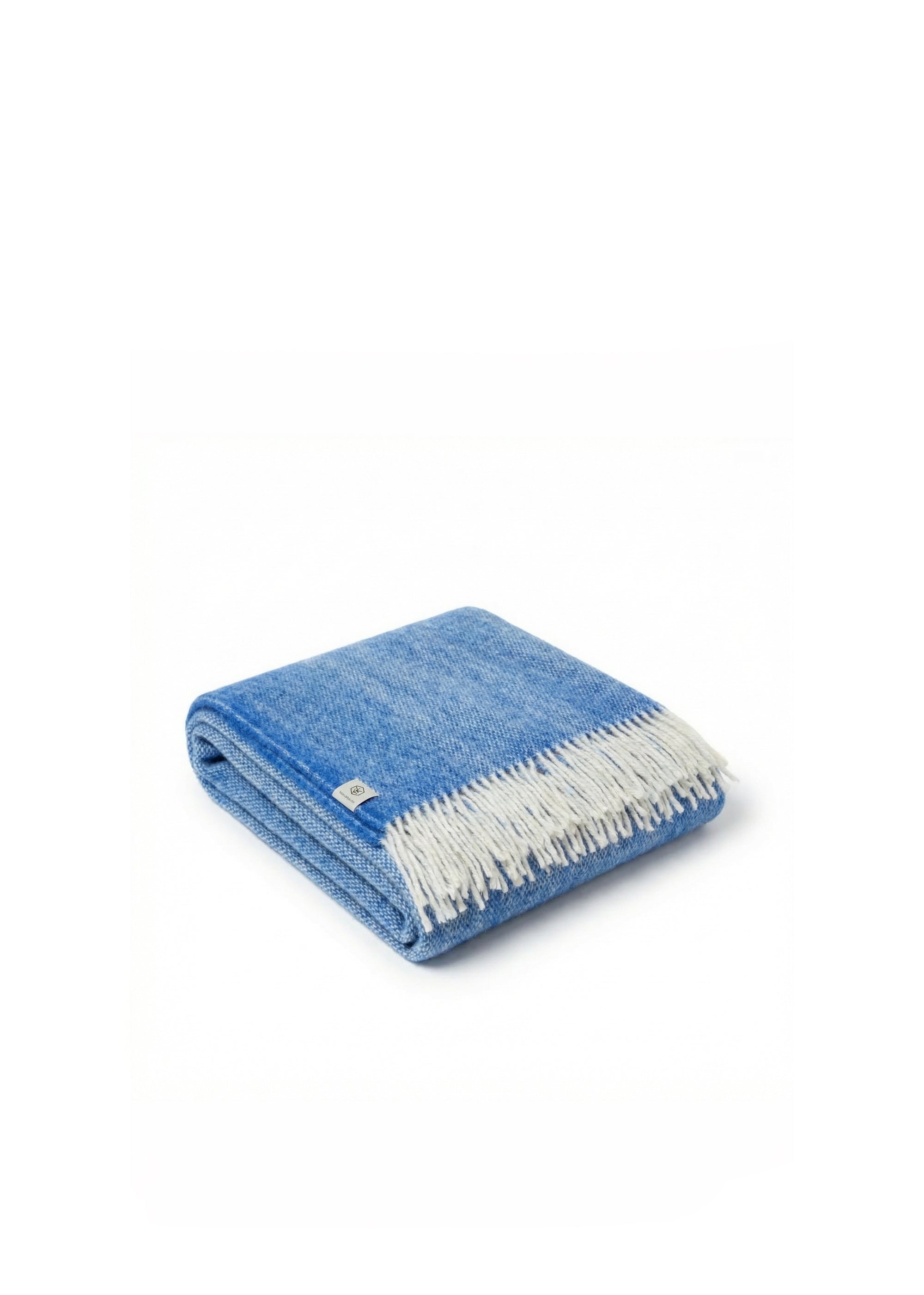 Couverture en laine bleue et blanche avec franges, posée sur un canapé rembourré foncé.